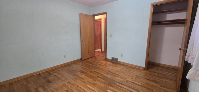 unfurnished bedroom with a closet, visible vents, baseboards, and wood finished floors