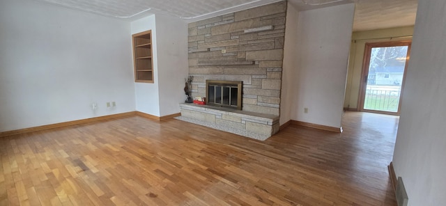 unfurnished living room with baseboards, wood finished floors, and a stone fireplace