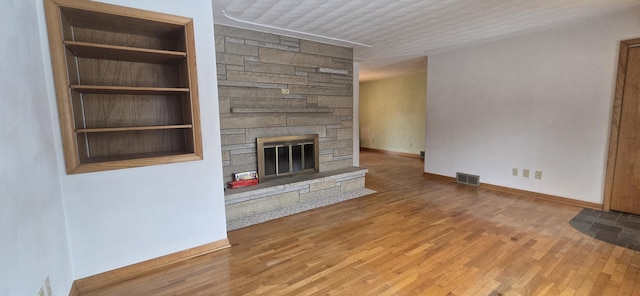 unfurnished living room featuring built in shelves, a fireplace, visible vents, and wood finished floors