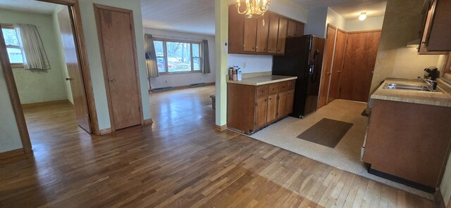 kitchen with light countertops, black refrigerator with ice dispenser, a sink, and light wood-style flooring