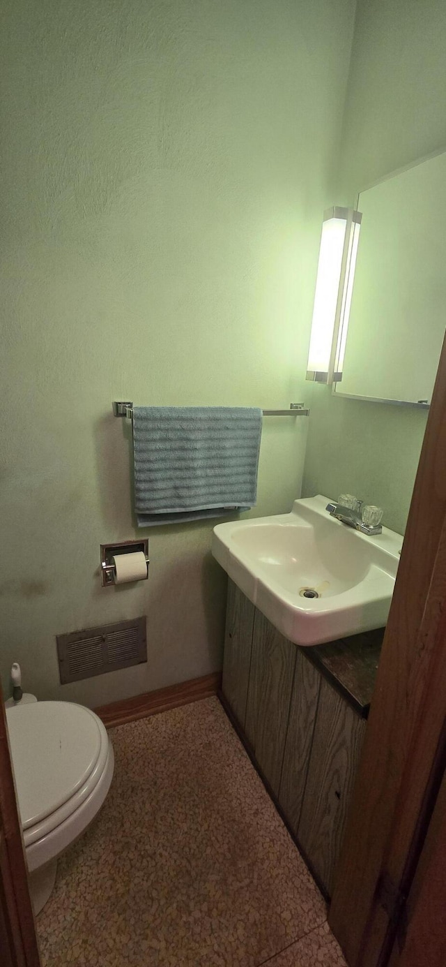 half bathroom with baseboards, vanity, and toilet