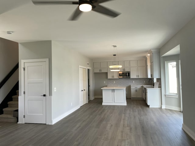 kitchen with light countertops, stainless steel microwave, decorative backsplash, a sink, and wood finished floors