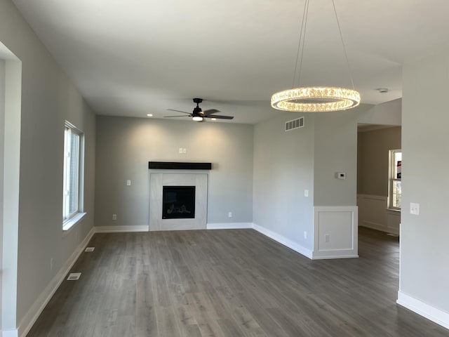 unfurnished living room featuring dark wood-type flooring, visible vents, a fireplace, and ceiling fan with notable chandelier