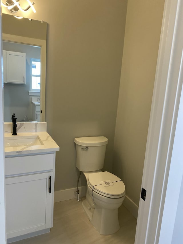 half bath with baseboards, vanity, and toilet