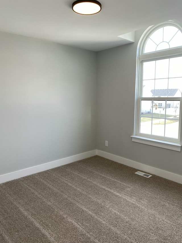 empty room with baseboards, visible vents, and dark colored carpet