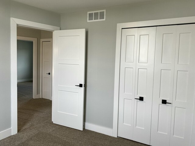 unfurnished bedroom featuring dark colored carpet, a closet, visible vents, and baseboards