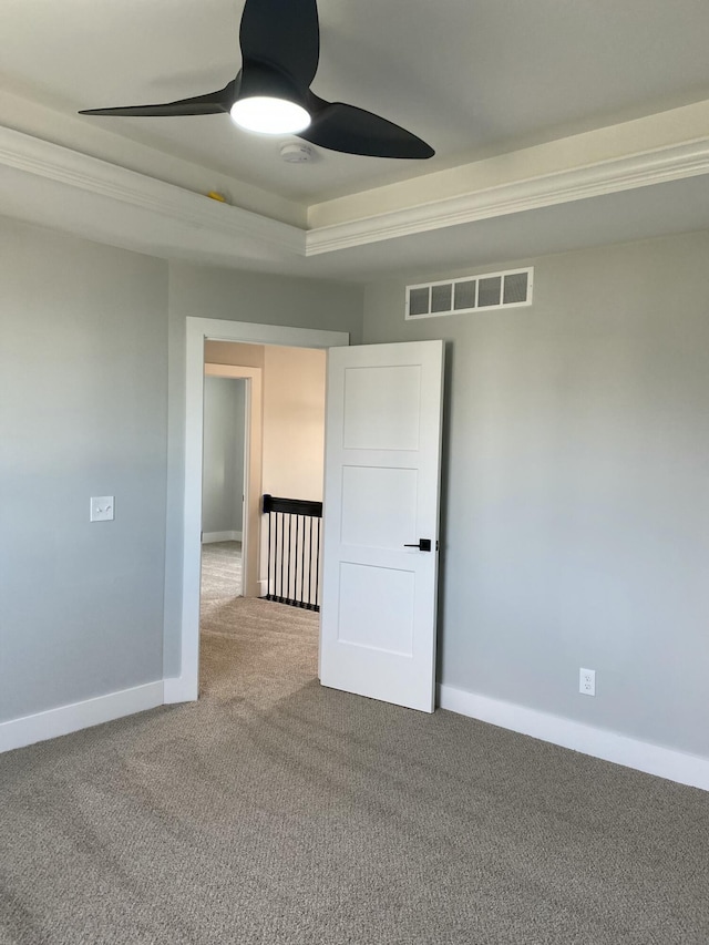 spare room featuring ceiling fan, visible vents, baseboards, a tray ceiling, and carpet