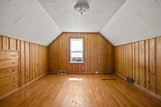 bonus room with vaulted ceiling, visible vents, wood walls, and hardwood / wood-style flooring