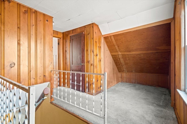 additional living space with vaulted ceiling, light colored carpet, and wooden walls