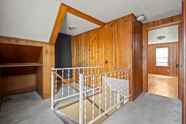 corridor featuring light carpet, wood walls, and an upstairs landing