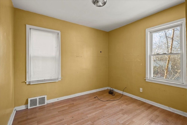 empty room featuring light wood finished floors, visible vents, and baseboards