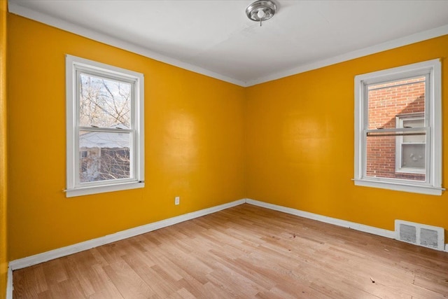 empty room featuring light wood-type flooring, baseboards, visible vents, and ornamental molding