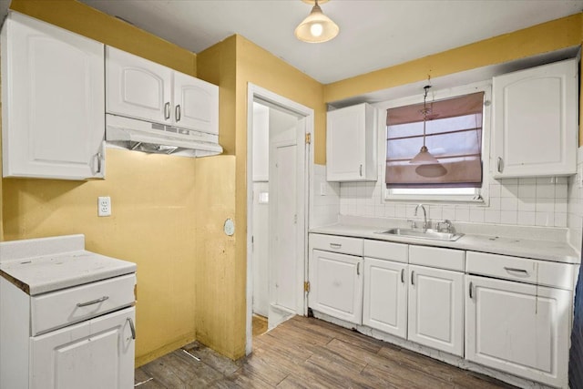 kitchen with under cabinet range hood, a sink, white cabinetry, light countertops, and pendant lighting