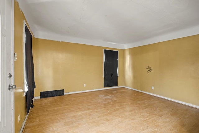 empty room featuring wood finished floors, visible vents, and baseboards