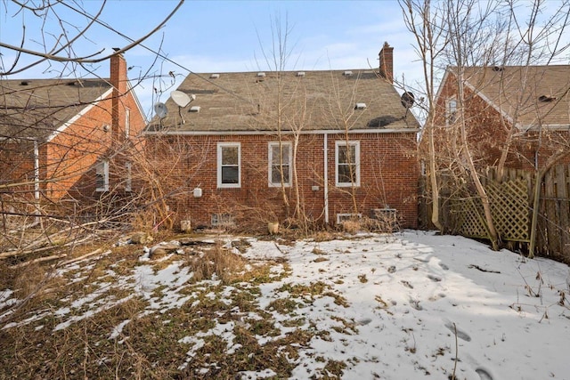 snow covered property featuring roof with shingles, brick siding, and a chimney