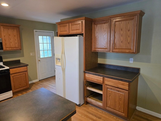 kitchen featuring light wood-type flooring, white appliances, dark countertops, and brown cabinets