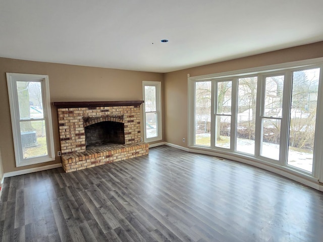 unfurnished living room with a brick fireplace, dark wood-style flooring, and plenty of natural light