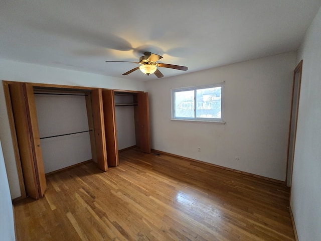 unfurnished bedroom with light wood-type flooring, a ceiling fan, and two closets