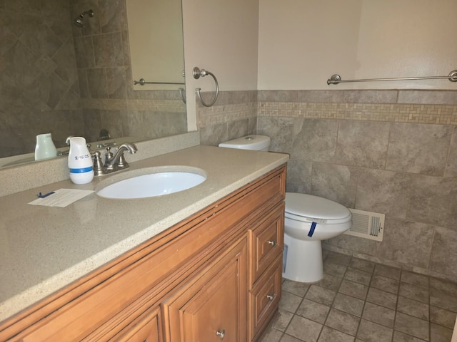 bathroom with visible vents, toilet, tile patterned flooring, vanity, and tile walls