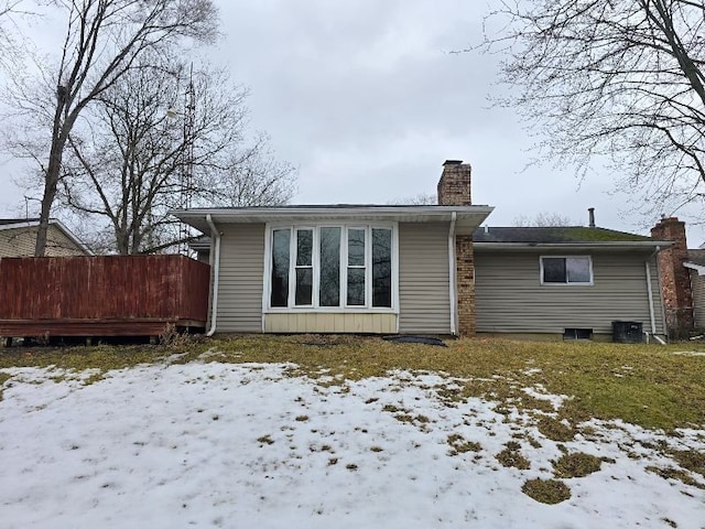 snow covered house with cooling unit, fence, and a chimney