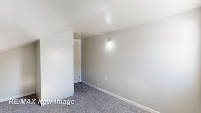 additional living space featuring vaulted ceiling, baseboards, and dark colored carpet