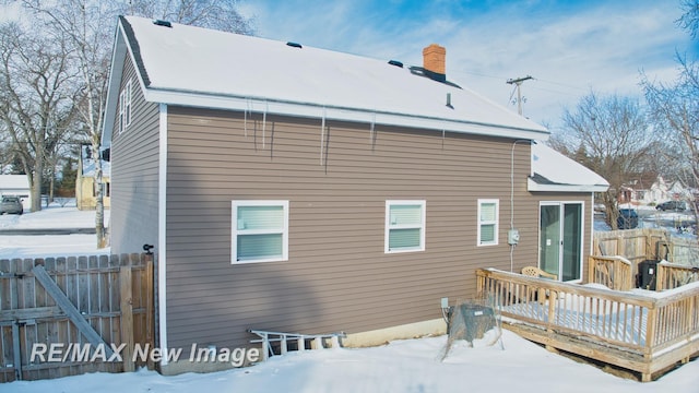 snow covered rear of property featuring a chimney, fence, and a wooden deck