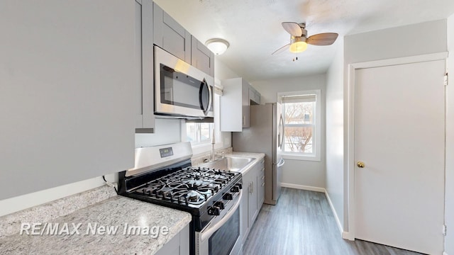 kitchen with light wood-style flooring, gray cabinetry, appliances with stainless steel finishes, a ceiling fan, and baseboards