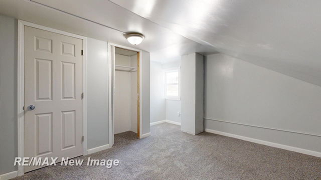 unfurnished bedroom featuring light carpet, a closet, lofted ceiling, and baseboards