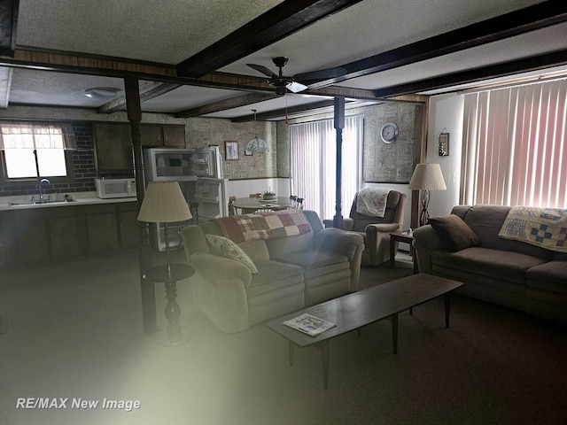 living room with ceiling fan, a textured ceiling, plenty of natural light, and beam ceiling