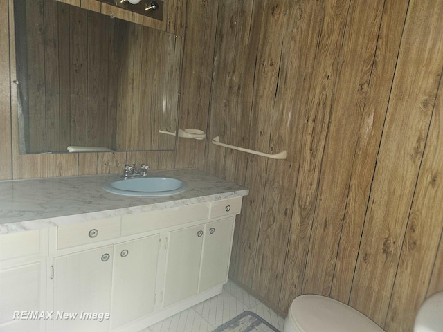 bathroom featuring toilet, wood walls, and vanity