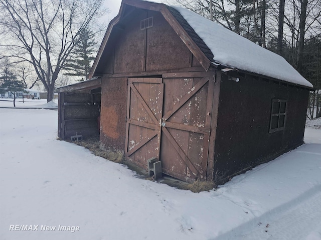 snow covered structure with a garage, an outdoor structure, and a barn