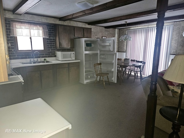 kitchen with light countertops, white microwave, dark brown cabinetry, a sink, and beamed ceiling