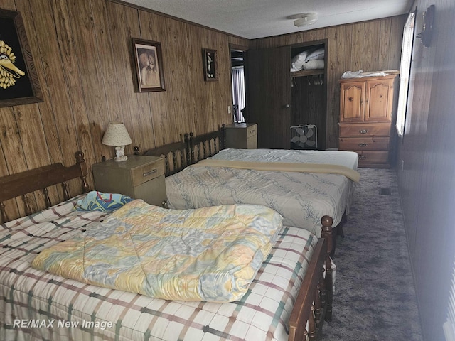 bedroom featuring wooden walls, dark carpet, and a textured ceiling