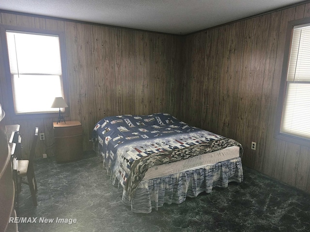 bedroom with dark colored carpet, multiple windows, and wooden walls