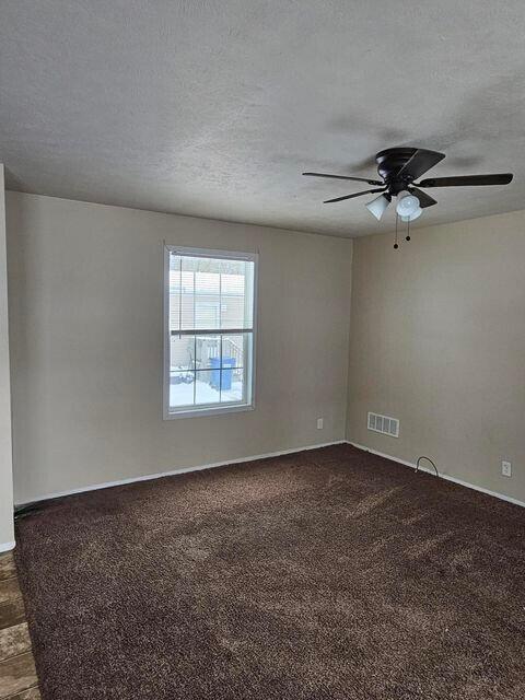 spare room with visible vents, dark carpet, a textured ceiling, and ceiling fan