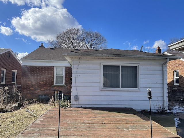 back of house featuring roof with shingles, a chimney, a deck, and brick siding