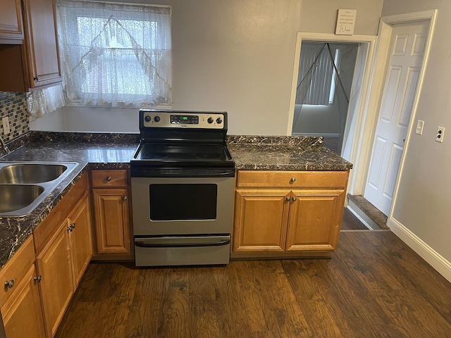 kitchen with dark countertops, brown cabinetry, dark wood-type flooring, stainless steel range with electric cooktop, and a sink