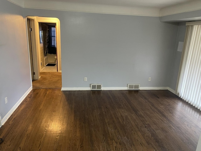 empty room with dark wood-style floors, visible vents, and baseboards