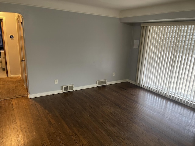 empty room with baseboards, visible vents, arched walkways, and dark wood finished floors