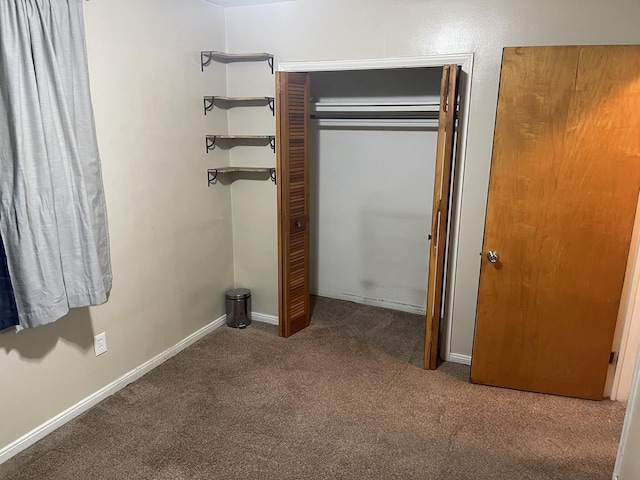 unfurnished bedroom with dark colored carpet, a closet, and baseboards