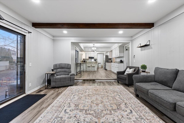 living room featuring a chandelier, beam ceiling, light wood-style flooring, and baseboards