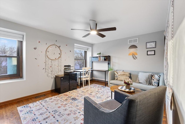 living area with visible vents, ceiling fan, baseboards, and wood finished floors