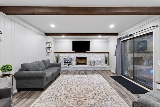 living room featuring a brick fireplace, beam ceiling, and wood finished floors