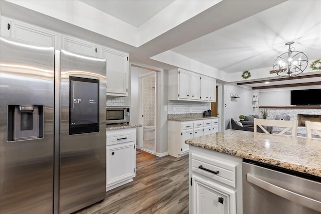 kitchen with stainless steel appliances, white cabinetry, hanging light fixtures, and backsplash