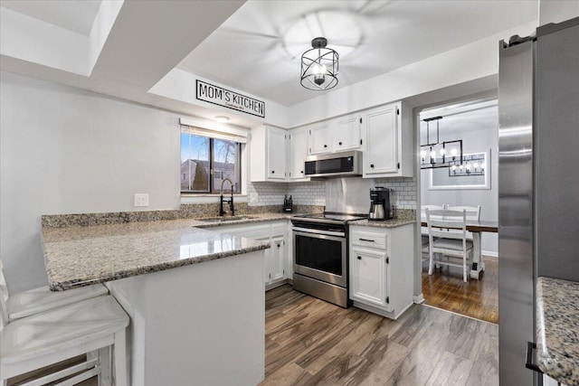 kitchen with light stone counters, a peninsula, stainless steel appliances, white cabinetry, and a sink