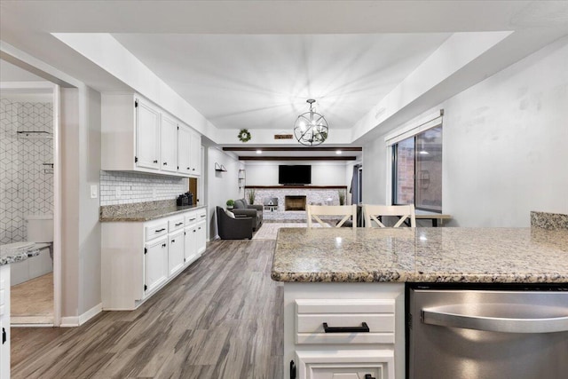 kitchen featuring tasteful backsplash, white cabinets, dishwasher, light stone countertops, and a fireplace