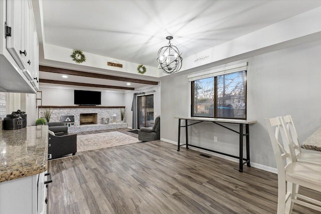 living area featuring visible vents, baseboards, dark wood-style flooring, an inviting chandelier, and a fireplace