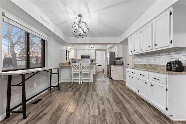 kitchen with tasteful backsplash, white cabinets, dark wood finished floors, decorative light fixtures, and light stone countertops