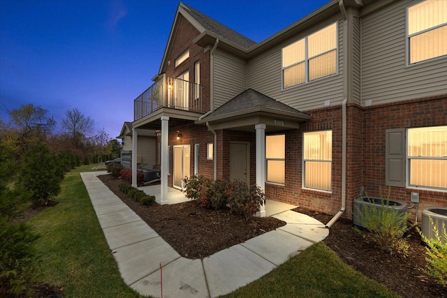 exterior space featuring brick siding, roof with shingles, a front yard, central AC, and a balcony