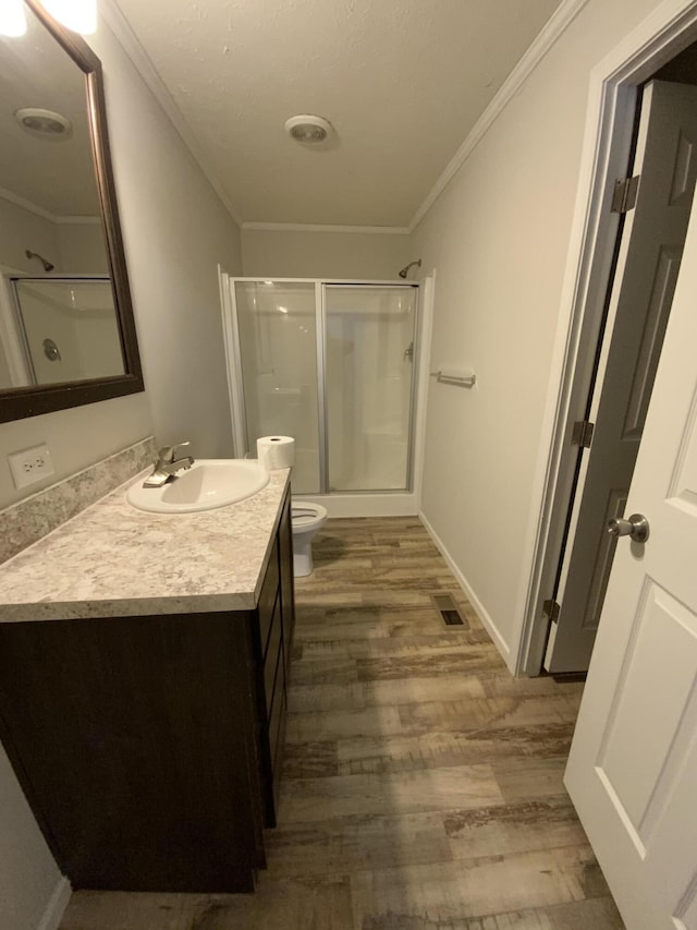 bathroom with toilet, wood finished floors, crown molding, vanity, and a shower stall